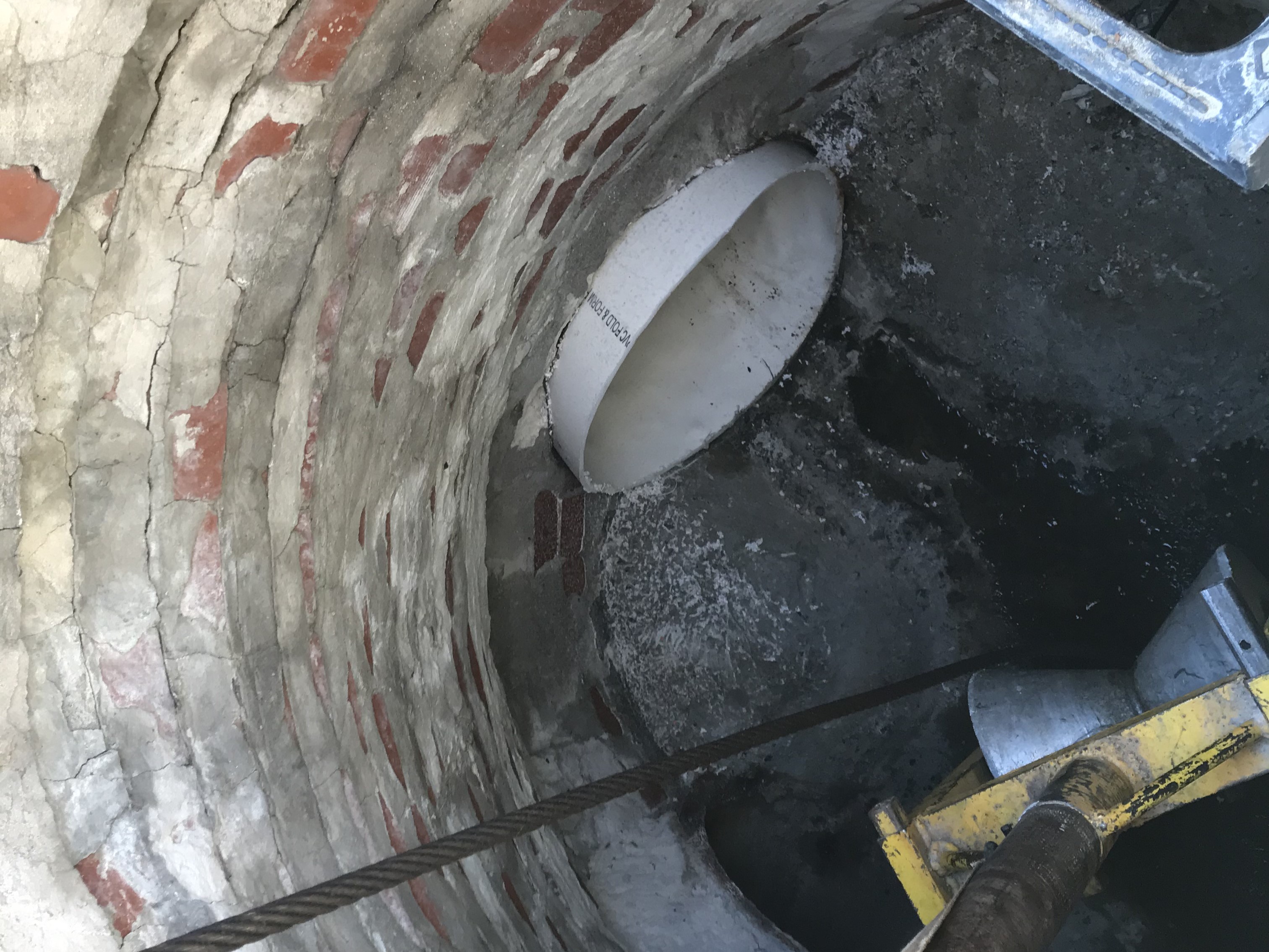 An image of the inside of a manhole cover where a winch cable is being used to pull the white PVC liner through the pipe
